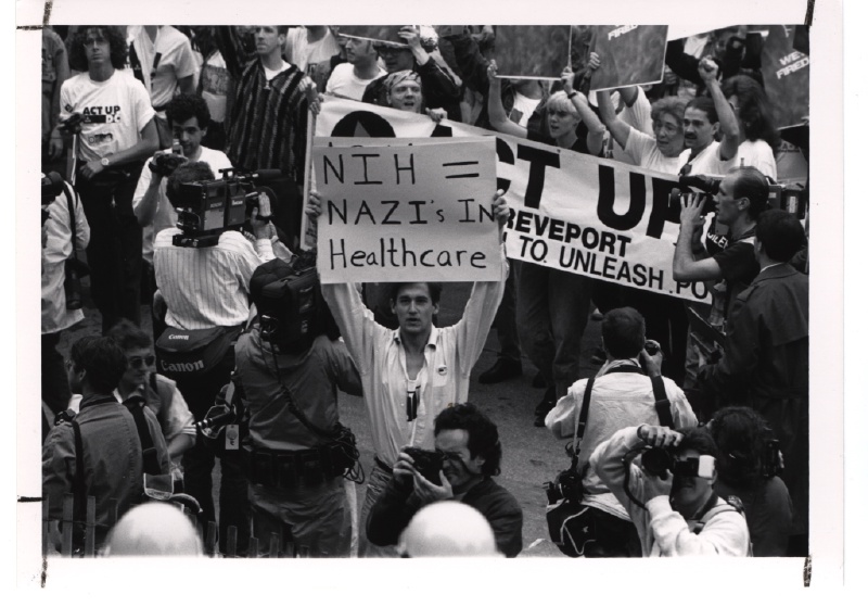 Attivisti del movimento ACT UP durante una protesta presso i National Institutes of Health statunitensi nel maggio 1990. Foto: [NIH History Office / Wikimedia Commons](https://commons.wikimedia.org/wiki/File:ACT_UP_Activists_at_the_National_Institutes_of_Health_(14359361475).jpg) (Pubblico dominio)