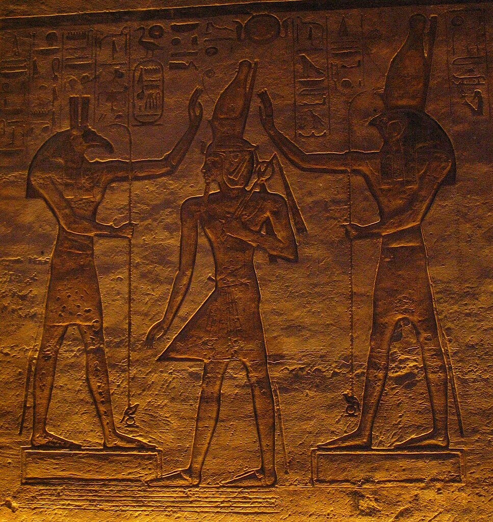 Set (à esquerda) e Hórus (à direita) colocam a coroa real na cabeça de Ramsés II. Baixo-relevo do Grande Templo de Abu Simbel, XIX dinastia.