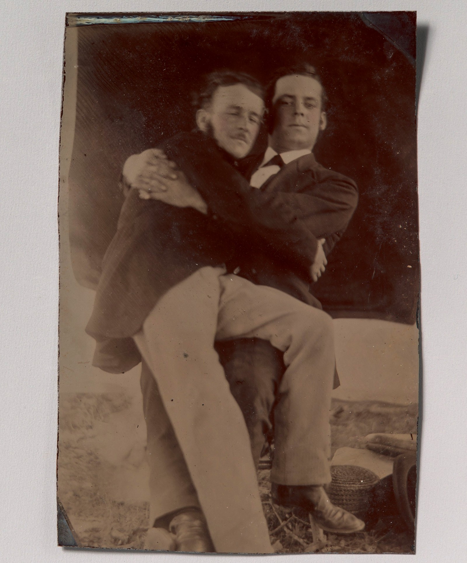 Dois homens abraçados, um sentado no colo do outro; ferrotipia de autor desconhecido, décadas de 1880–1890